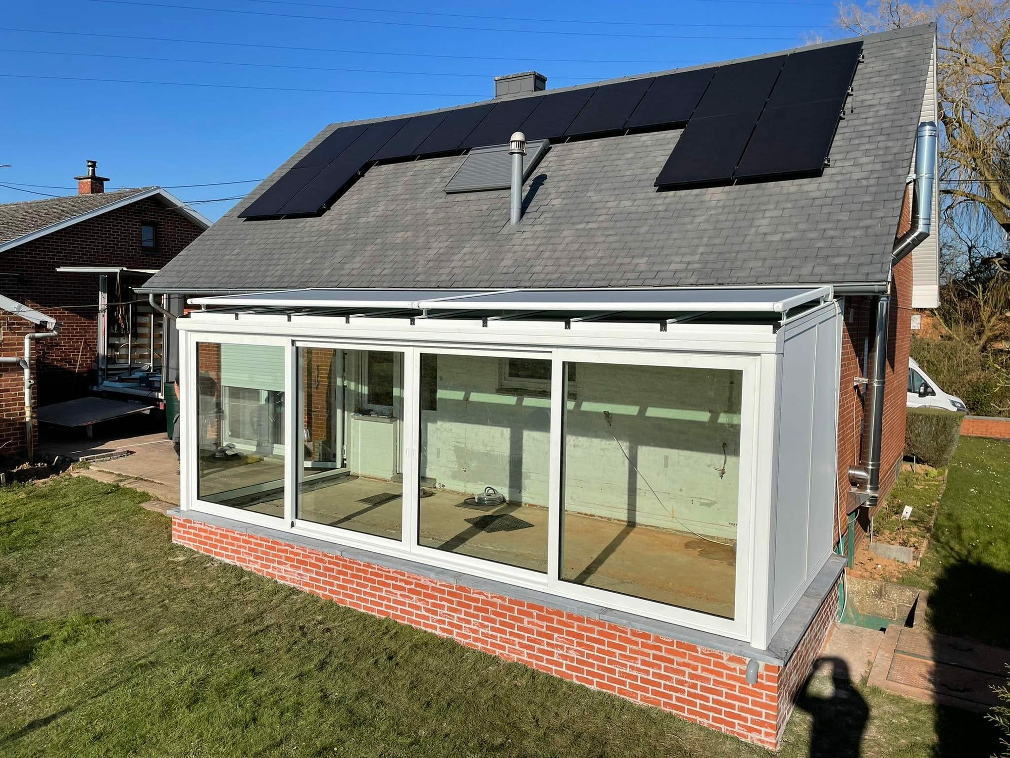 Véranda blanche à toiture opaque sur une maison en brique