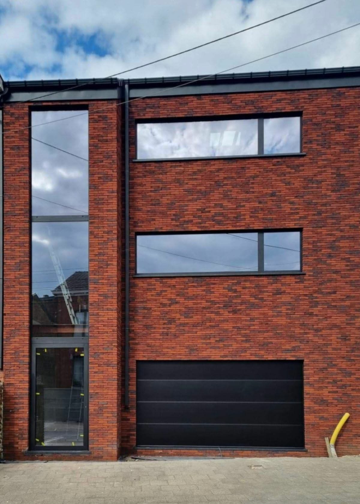 Maison étroite en brique avec vitrages superposés et porte de garage