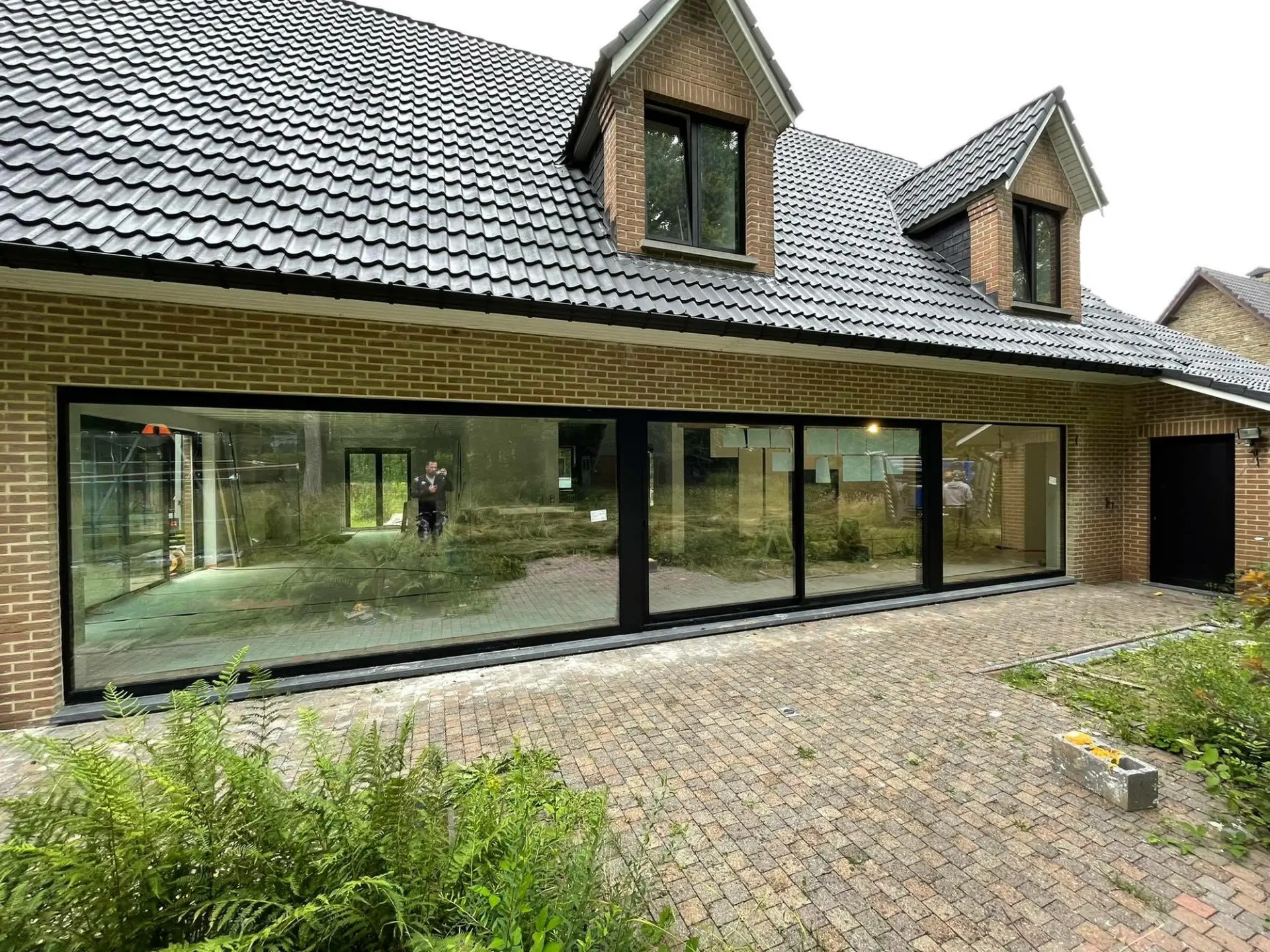 Façade en brique avec grande baie vitrée coulissante noire et porte d'entrée