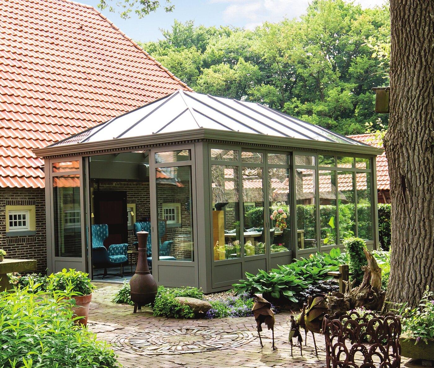 Véranda de style victorien en aluminium vert dans un jardin arboré