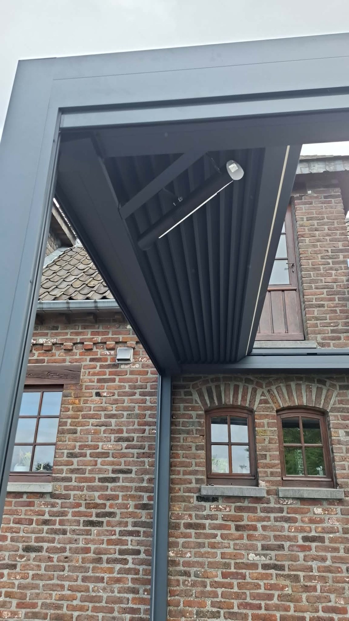 Détail de la structure d'une pergola à lames sur façade en brique