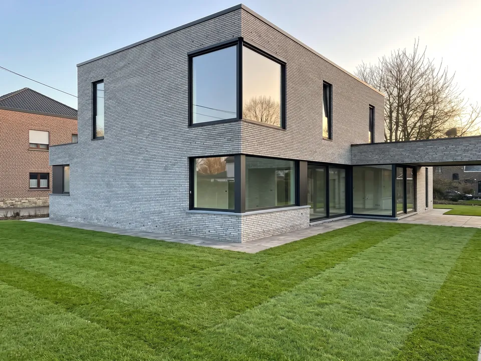 Après travaux — Maison contemporaine en brique claire avec de grandes baies vitrées aluminium noir et une pelouse neuve